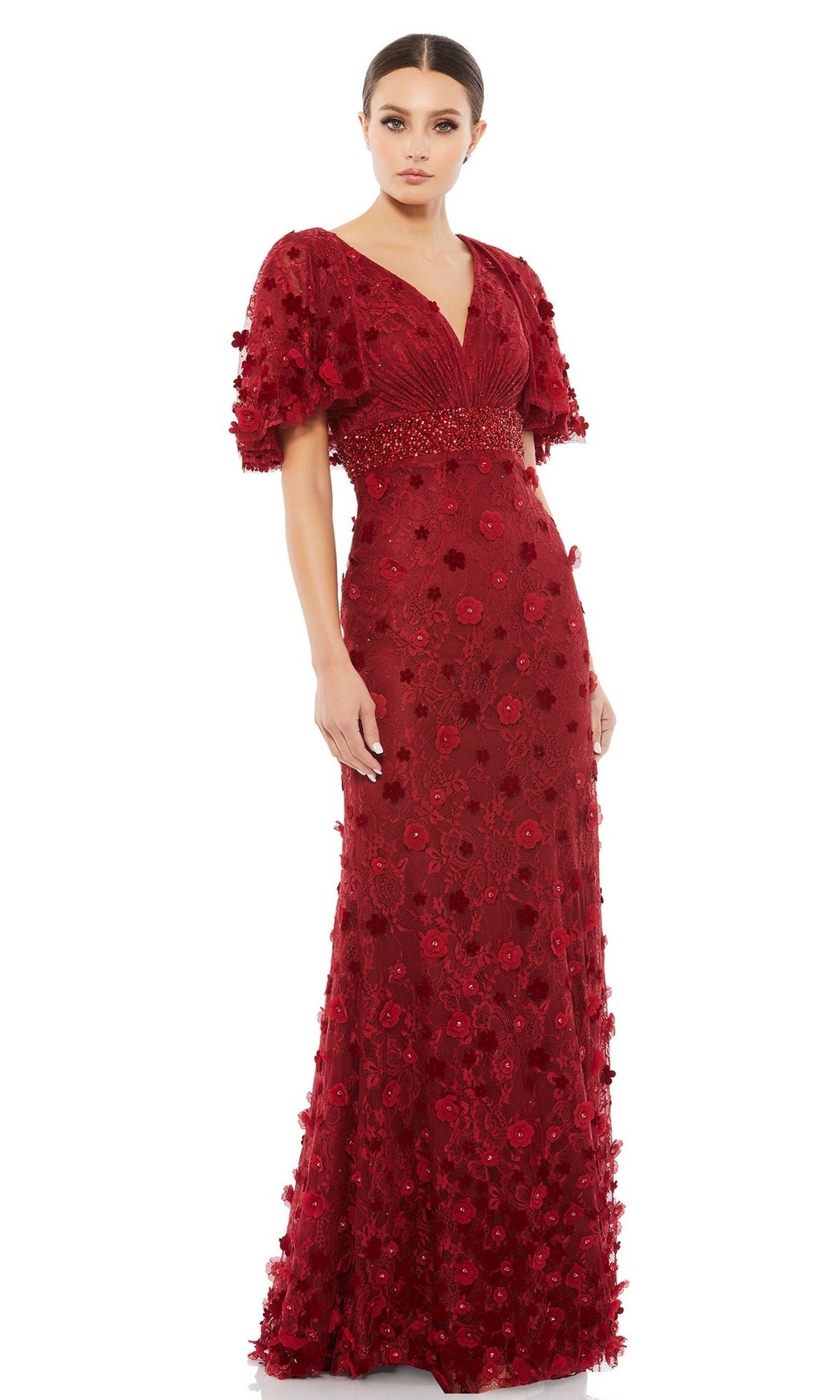A woman models the Mac Duggal 67712 short-sleeve long formal dress, featuring floral appliqué, a beaded waist, and puff sleeves in dark red, standing against a white background.